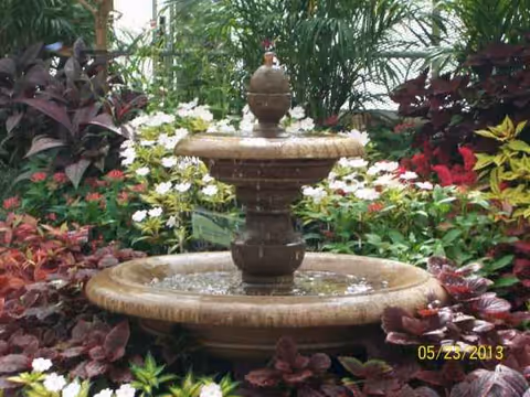A tiered fountain surrounded by colorful flowering plants in a lush outdoor garden.