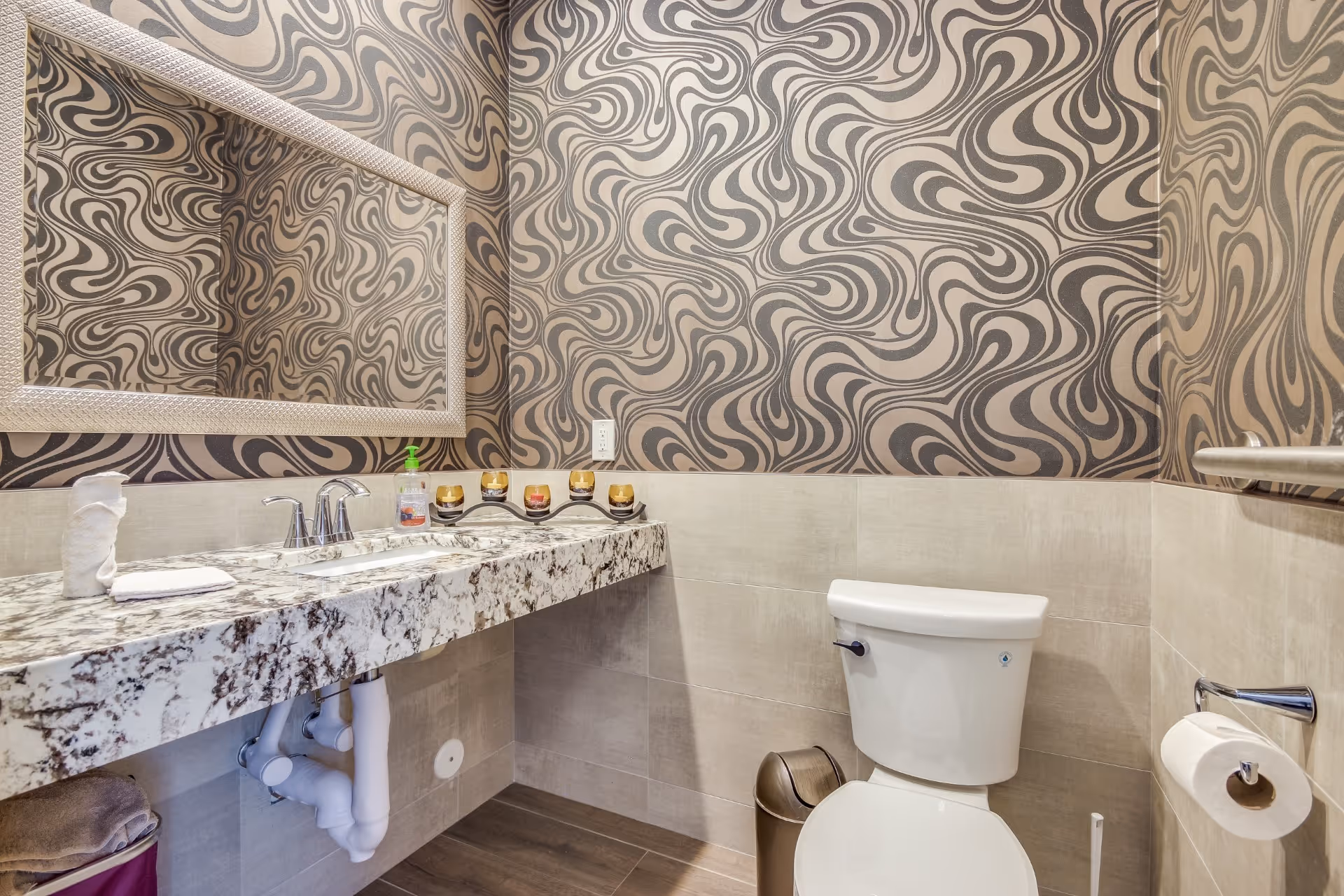 Modern restroom with a patterned wallpaper, marble countertop with sink and mirror, and a toilet.