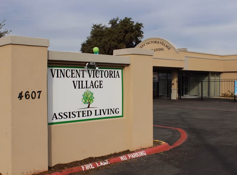 Exterior view of Vincent Victoria Village Assisted Living facility showing the entrance sign and part of the building with a parking area and a fire lane marked with no parking.
