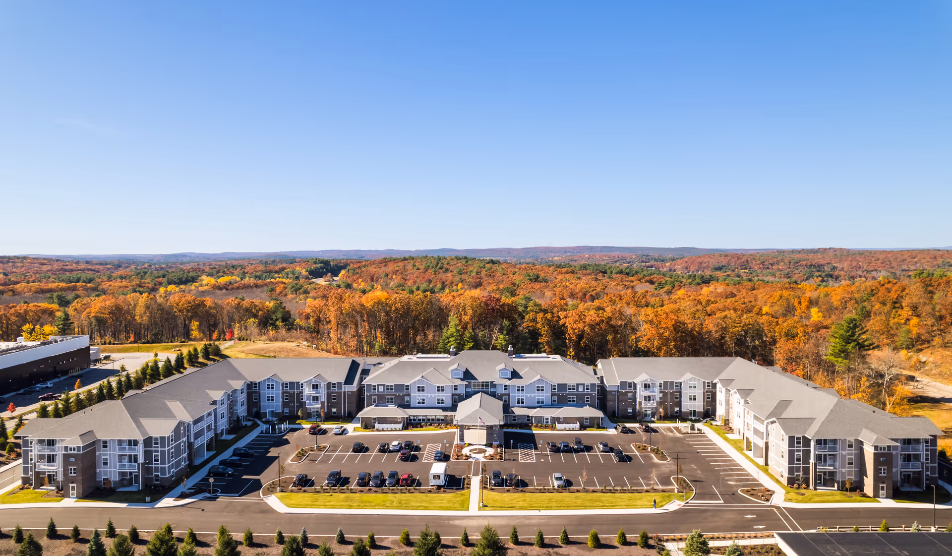 Aerial view of Pleasant Hill Retirement Community, a large U-shaped senior living building with parking lot surrounded by autumn trees.