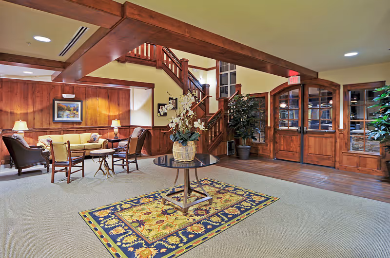 Lobby-style common area with a wooden staircase, seating area, and a central table with a floral arrangement on a patterned rug.