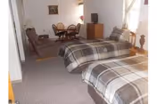 Studio-style room with two twin beds, an armchair, small dining table and a TV cabinet.
