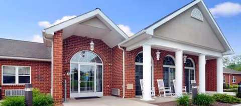 Brick senior living facility with arched glass doors, white columns, and rocking chairs on the entrance.