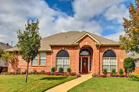 Brick senior living facility front with arched windows, entry door, and manicured lawn.