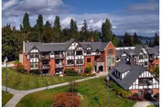A multi-building senior living campus with Tudor-style architecture, green lawns, and walking paths.