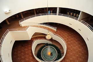 Top-down view of a multi-level indoor atrium with spiral balconies, a hanging chandelier, and a central fountain.