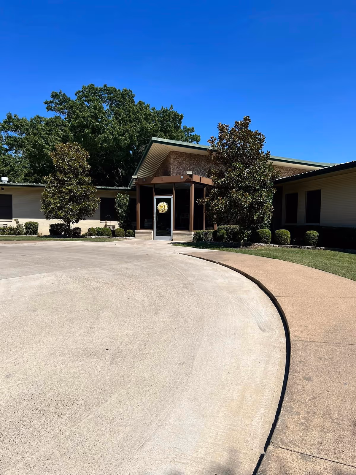 Front entrance of a single-story nursing and rehab center with a circular driveway, landscaping, and clear blue sky.