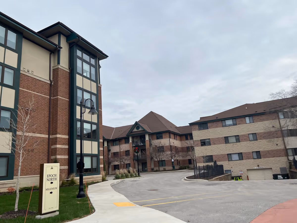 Front exterior of a multi-story senior living building with a driveway and a sign reading "EPOCH NORTH".