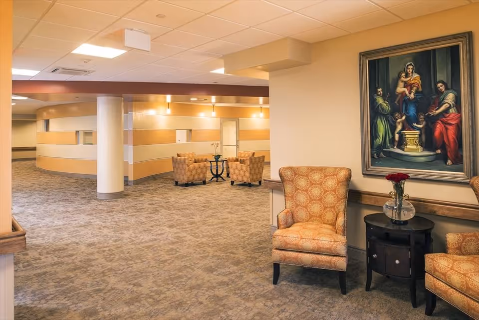 Spacious furnished hallway seating area with upholstered armchairs, side tables, and a large framed painting on the wall.