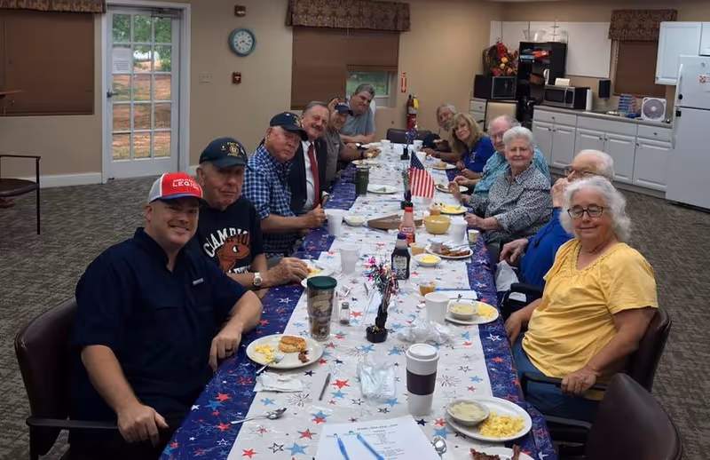 Seniors gathered around a long, festively decorated dining table in a community room enjoying a meal.