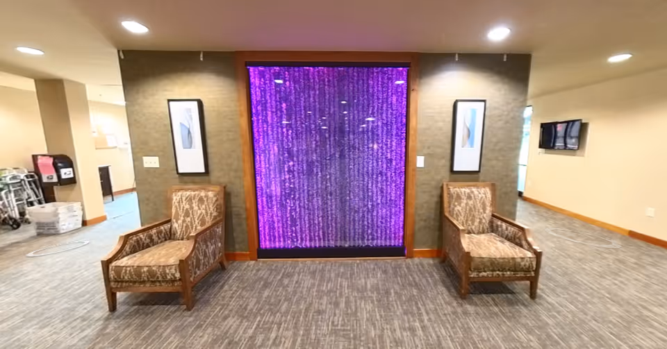 Lobby seating area with two upholstered chairs flanking a purple illuminated water-wall feature.