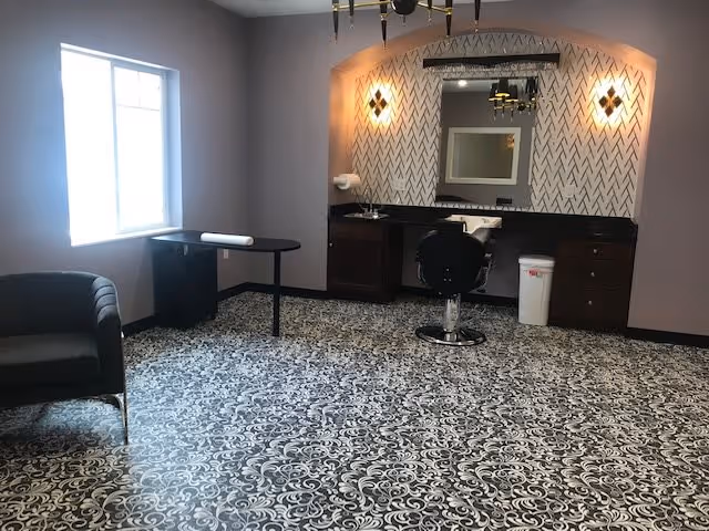 Room interior with a salon styling station including a chair, sink, mirror, patterned tile floor, and a window.