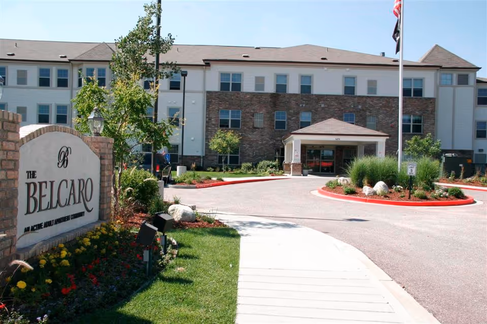 Front exterior view of The Belcaro senior living building with entrance and landscaped sign area.