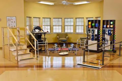 Interior rehabilitation gym at Villa Toscana at Cypress Woods with parallel bars and exercise equipment.