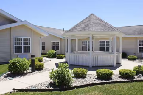 Single-story senior living facility exterior with a white gazebo and landscaped shrubs.