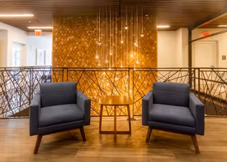 Two navy armchairs flank a small wooden table in a warmly lit seating area with a decorative wood-paneled wall and hanging pendant lights.