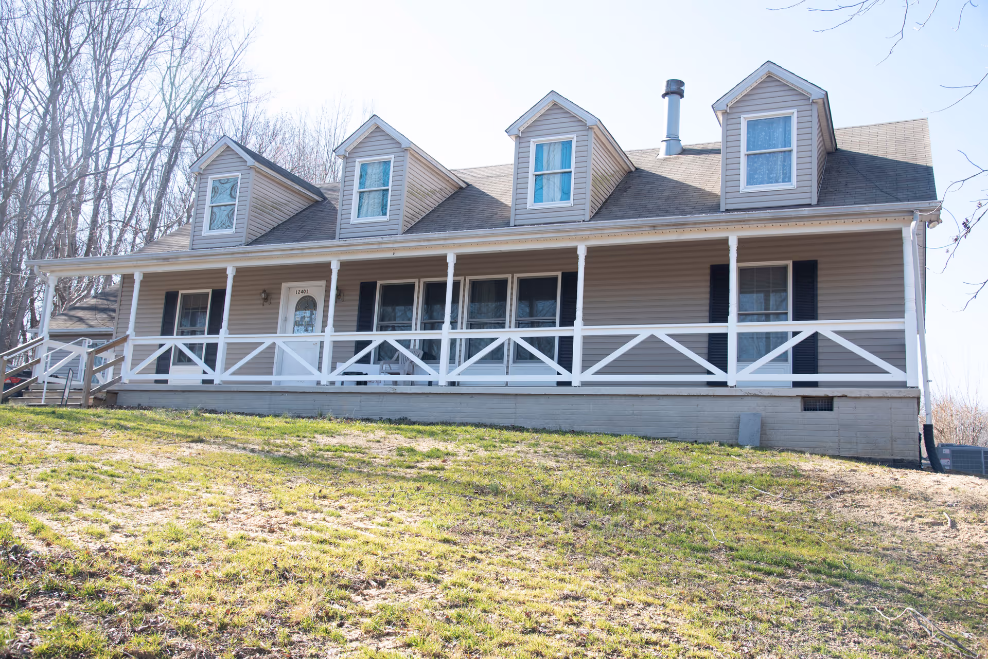 Front exterior of a house-style assisted living facility with wraparound porch and dormer windows.
