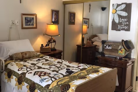 A cozy bedroom with a single bed covered by a floral quilt, bedside tables with lamps, mirrored closet doors, and decorative wall art.