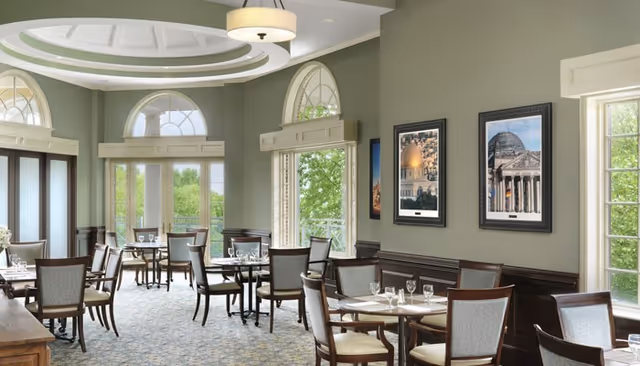 Elegant dining room with multiple set tables and chairs, large arched windows, and a decorative recessed ceiling.