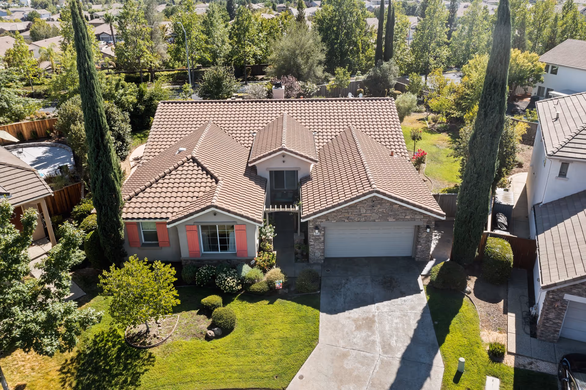 Aerial view of a single-story suburban house with a tiled roof, front lawn, and driveway leading to a two-car garage.