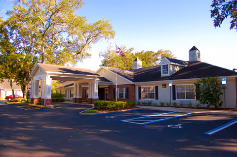 Single-story senior living facility building front with a covered entrance, American flag, and parking spaces including accessible spots.