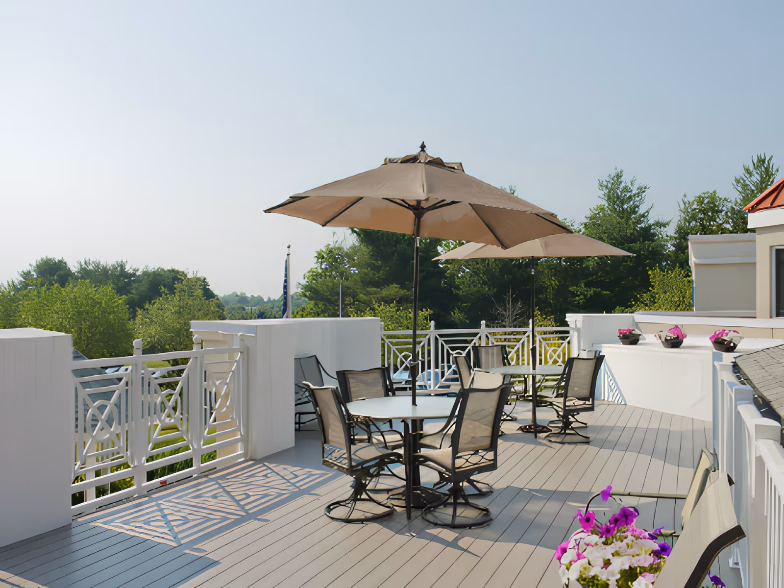Rooftop patio with round tables, chairs, large umbrellas and potted flowers overlooking trees.