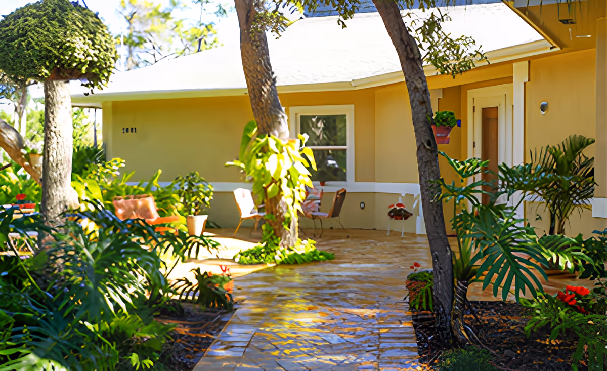 Front porch and garden walkway of a single-story residential building with potted plants and outdoor chairs.