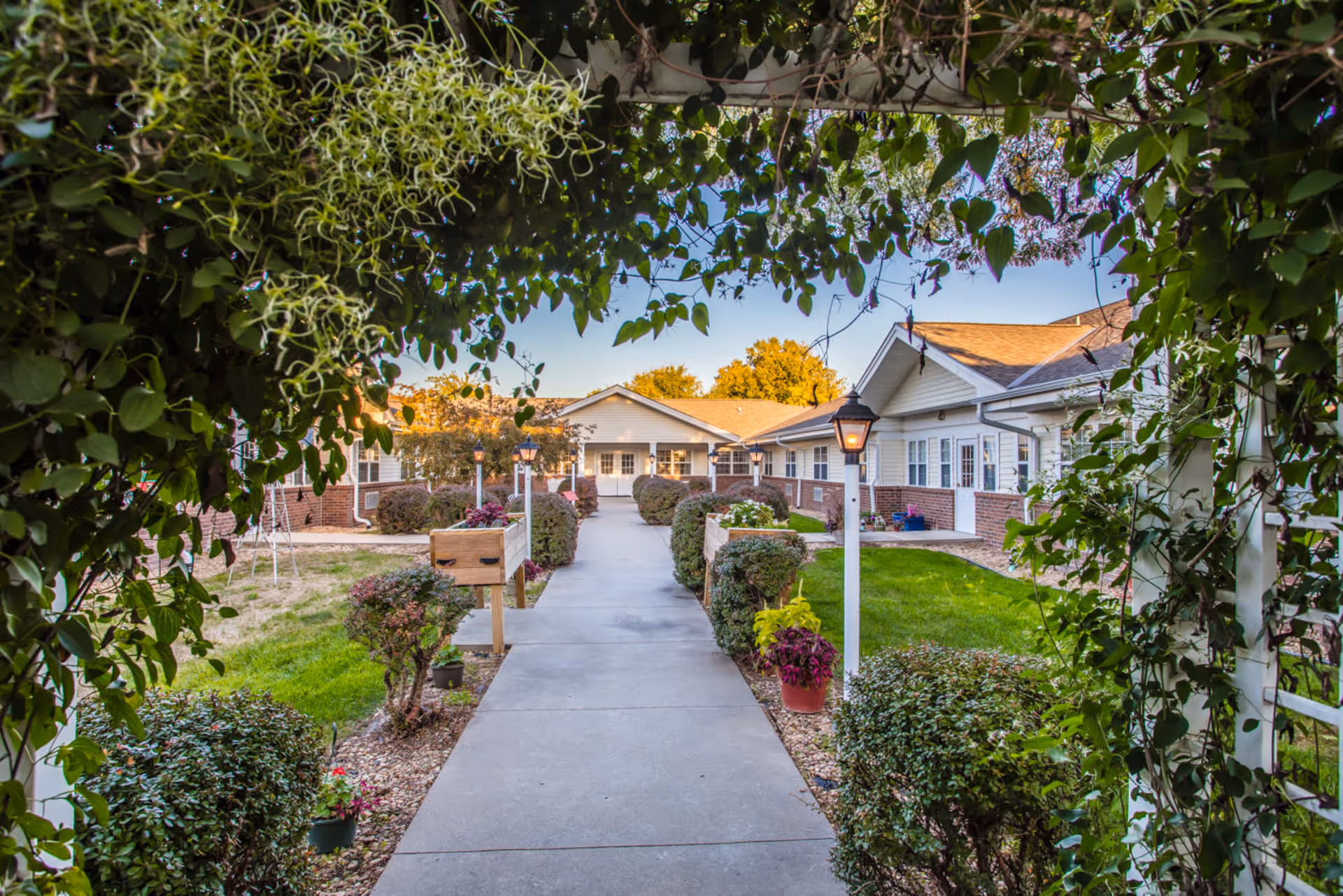 A paved walkway framed by a leafy trellis leads through a landscaped courtyard to the Homestead House buildings.