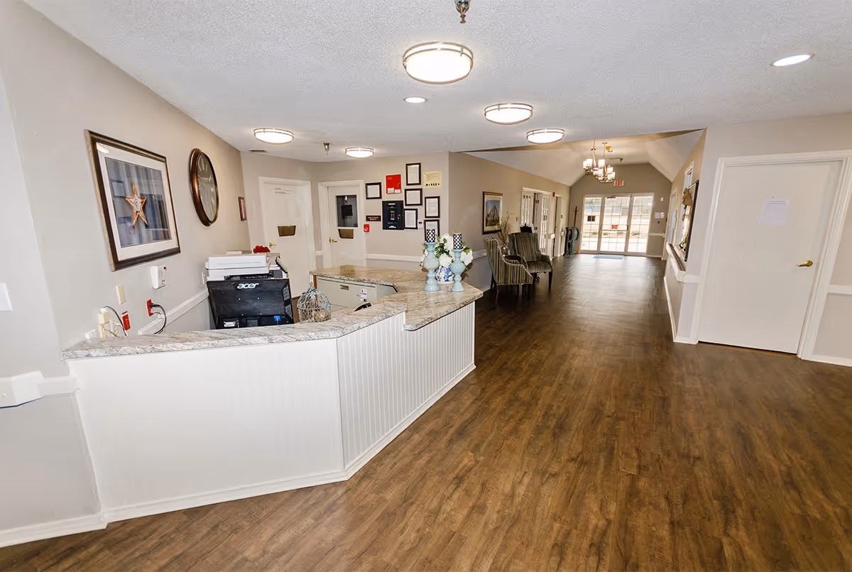 Reception desk and long lobby hallway with seating and wood-look flooring inside a senior living facility.