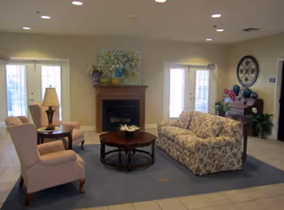 A comfortable common living area with a floral sofa, two armchairs, a central coffee table and a fireplace under artwork.
