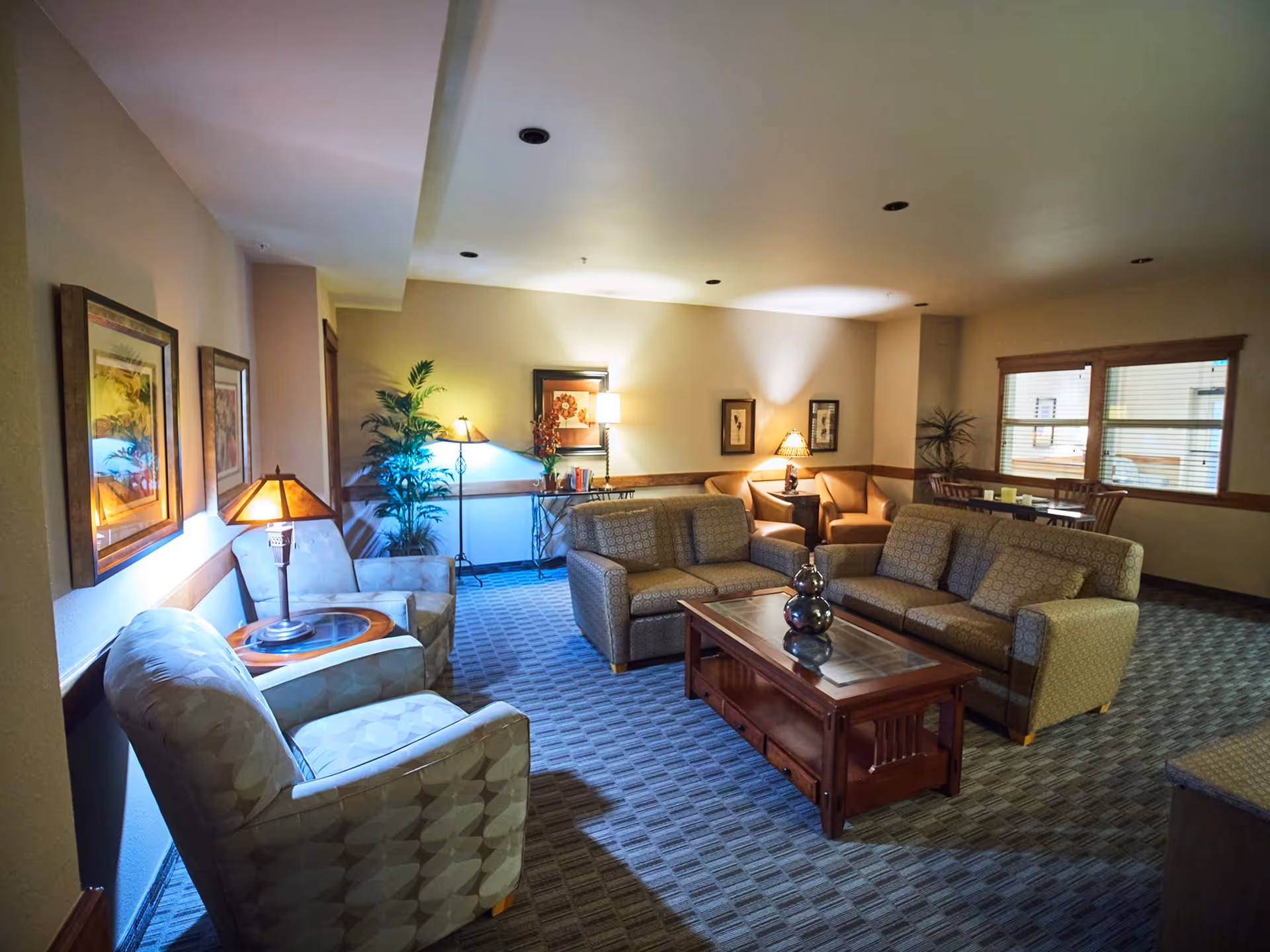 Spacious furnished common lounge with sofas, armchairs, coffee table, lamps, and framed artwork.