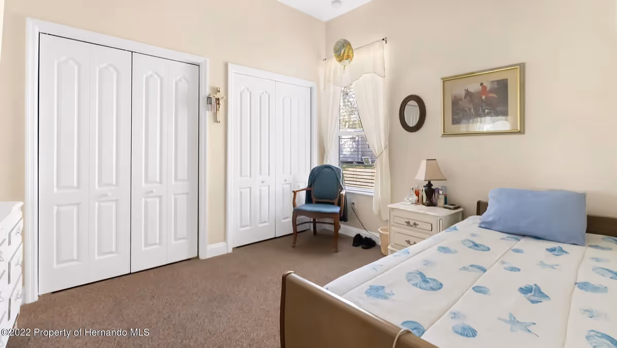 Sunny single-occupancy bedroom with a bed, nightstand, chair, window, and double closets.