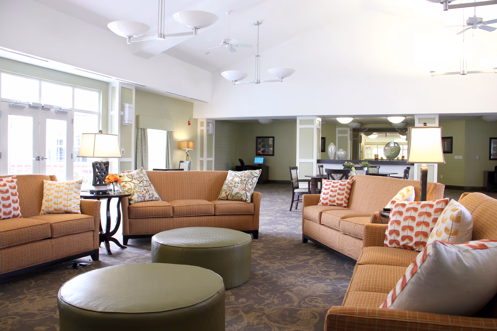 Bright communal lounge with several sofas, patterned throw pillows, round ottomans, side tables and lamps.