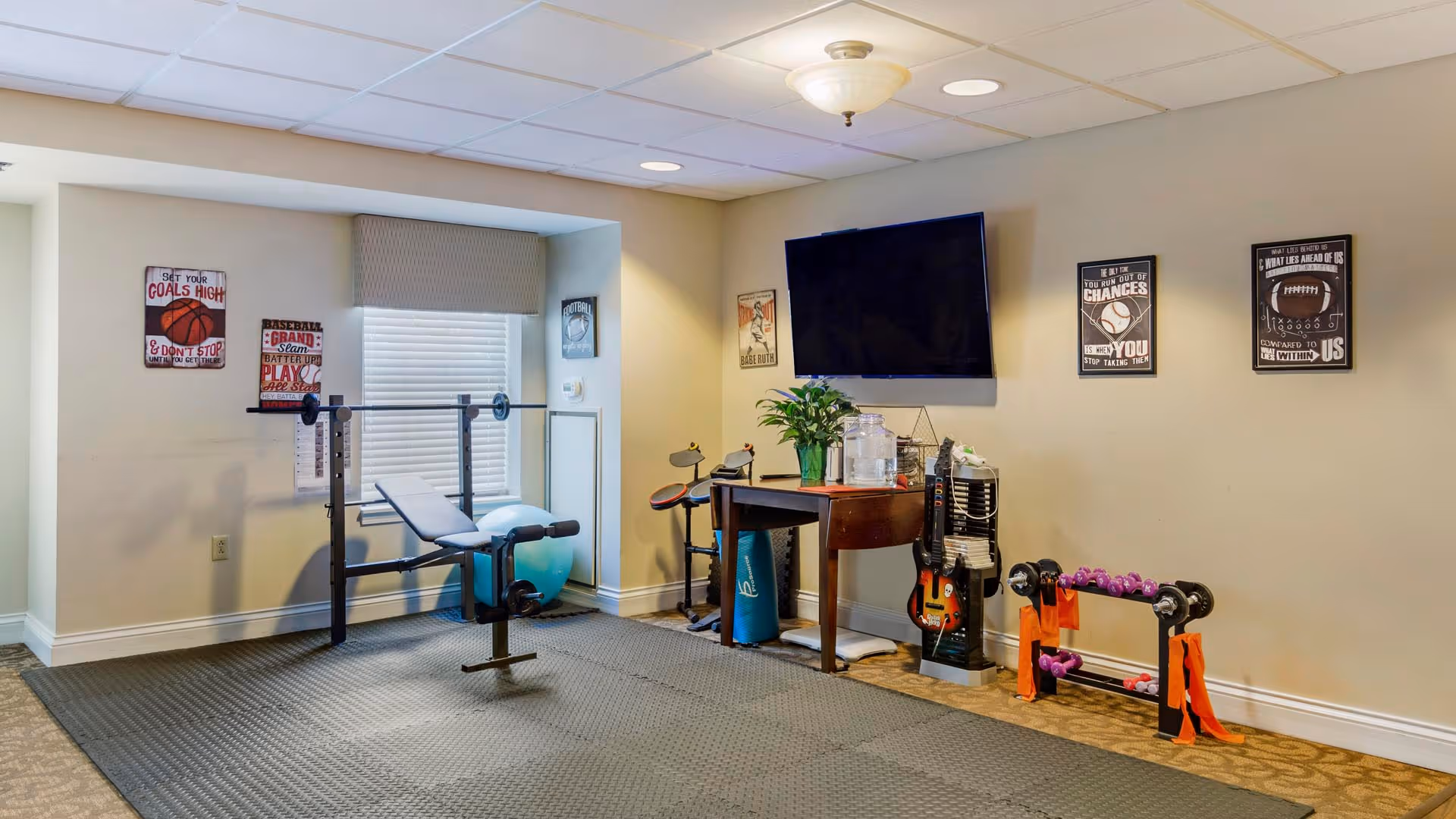Small exercise room with a weight bench, dumbbells, a TV mounted on the wall, and other workout equipment.