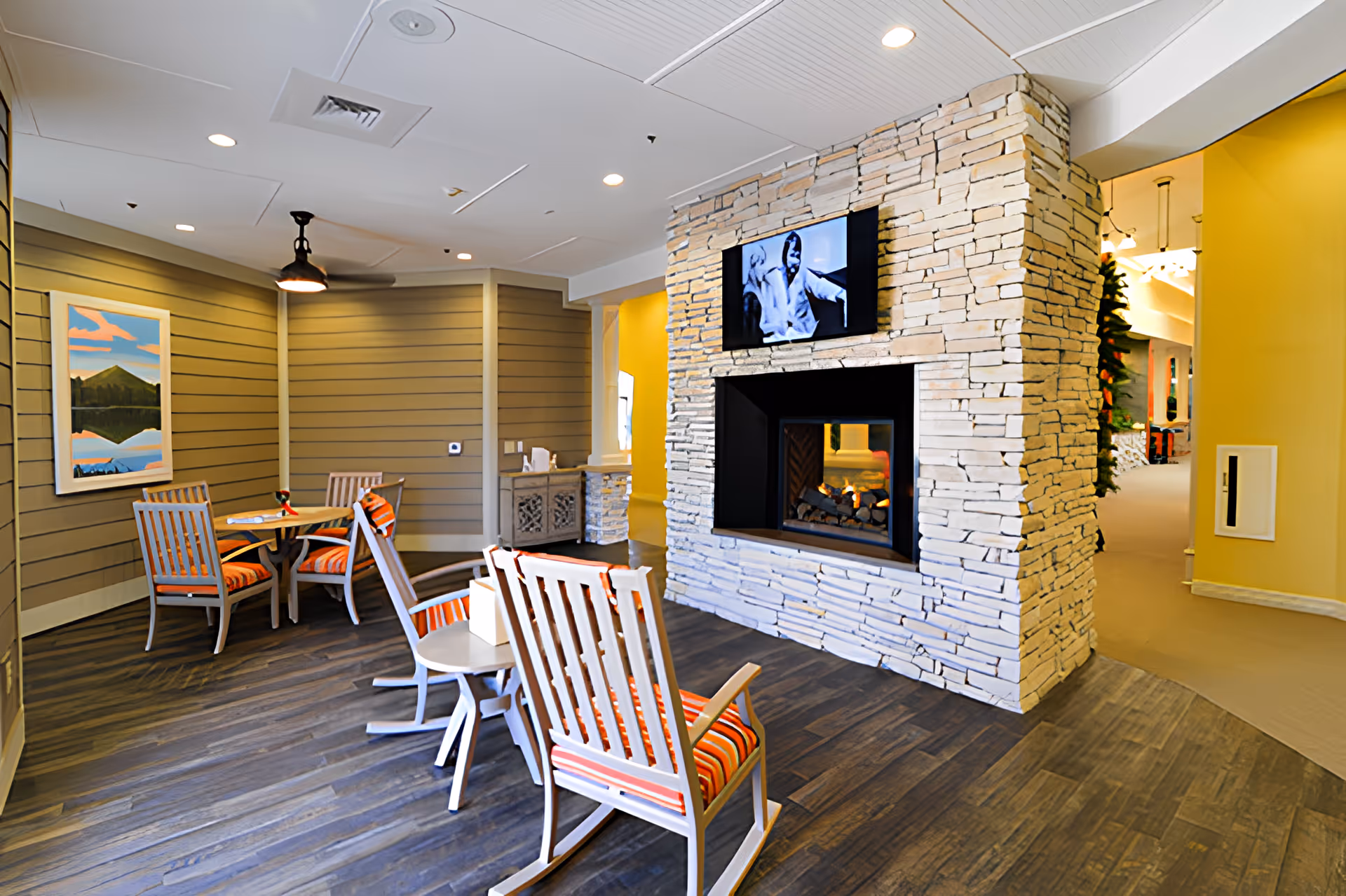 Common lounge area featuring a stone fireplace with a wall-mounted TV, round tables and striped cushioned chairs.