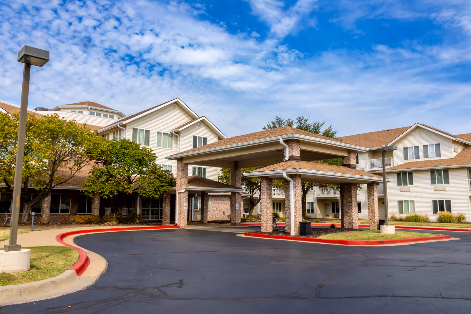 Exterior front entrance of a multi-story senior living facility with a covered porte-cochere and landscaped driveway.
