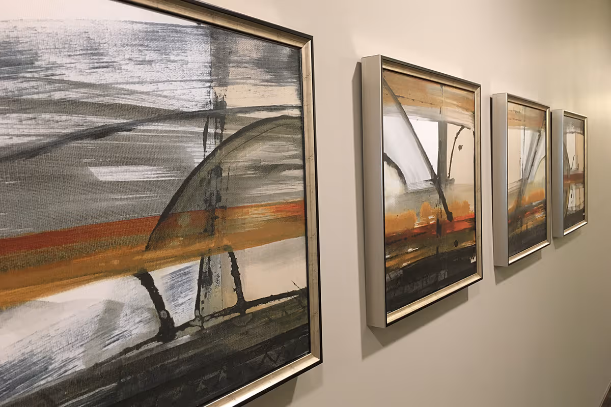 Four framed abstract paintings in silver frames hung in a row on an interior beige wall.