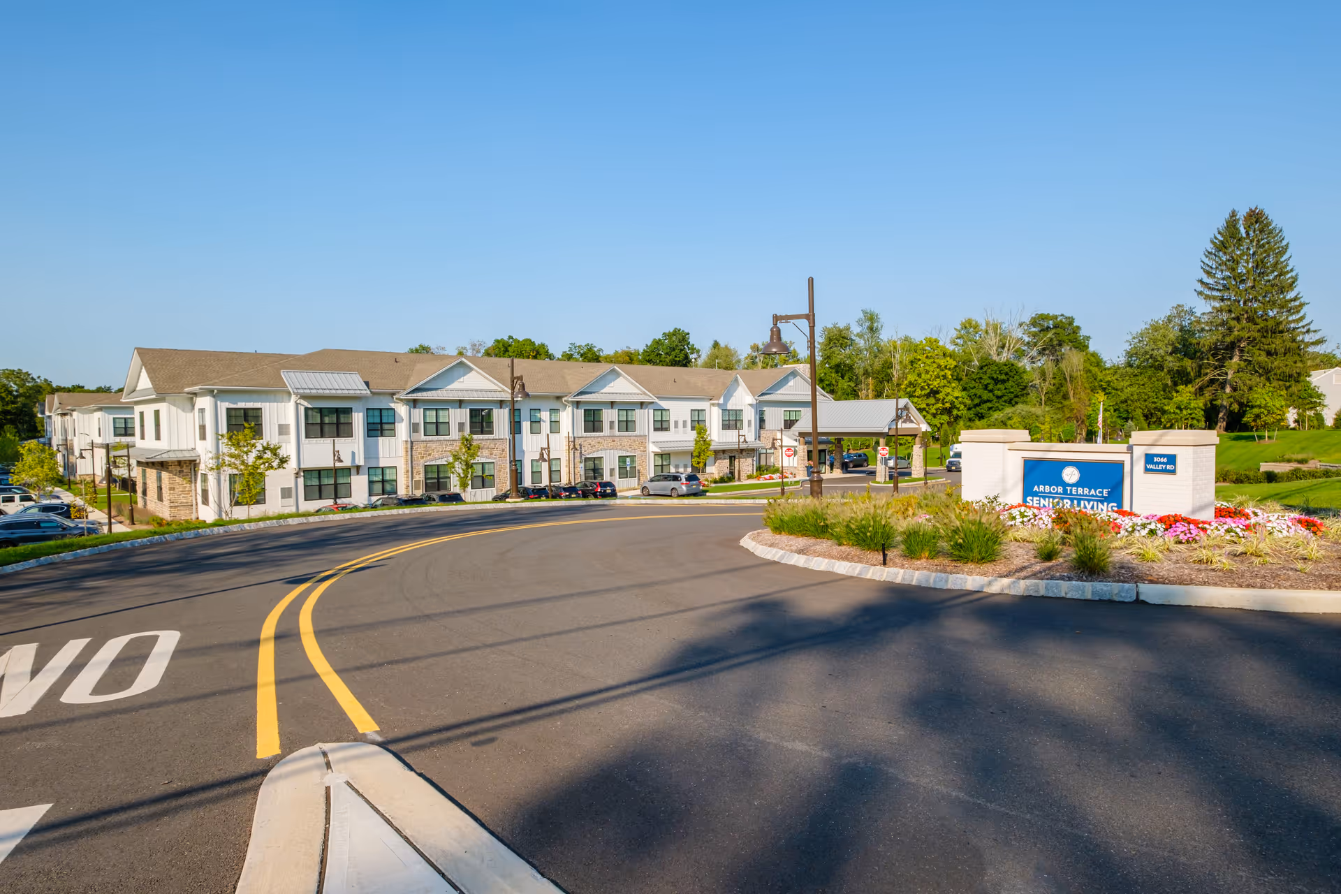 Front exterior of a two-story senior living community with a landscaped driveway and an 'Arbor Terrace Senior Living' sign.