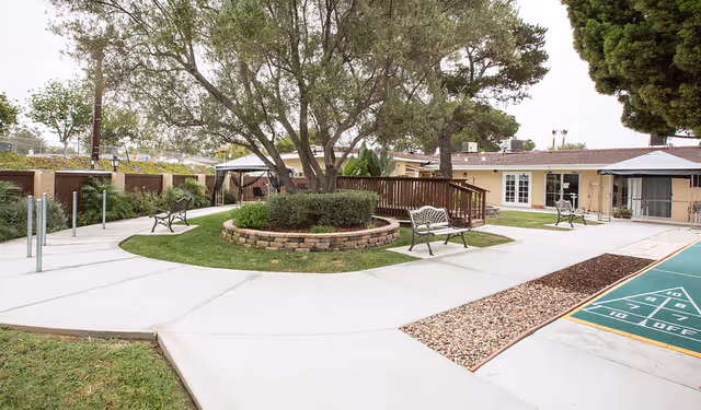 Courtyard with paved walkways, benches, a central tree planter, shuffleboard court and an adjacent single-story building.