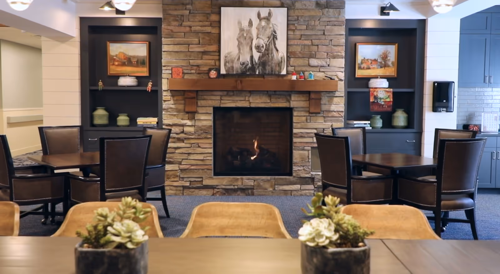 Communal dining area with a stone fireplace, round tables and chairs, and decorative shelving.