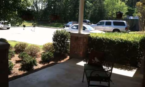 Outdoor patio with a chair, column, and trimmed hedges beside a parking lot.