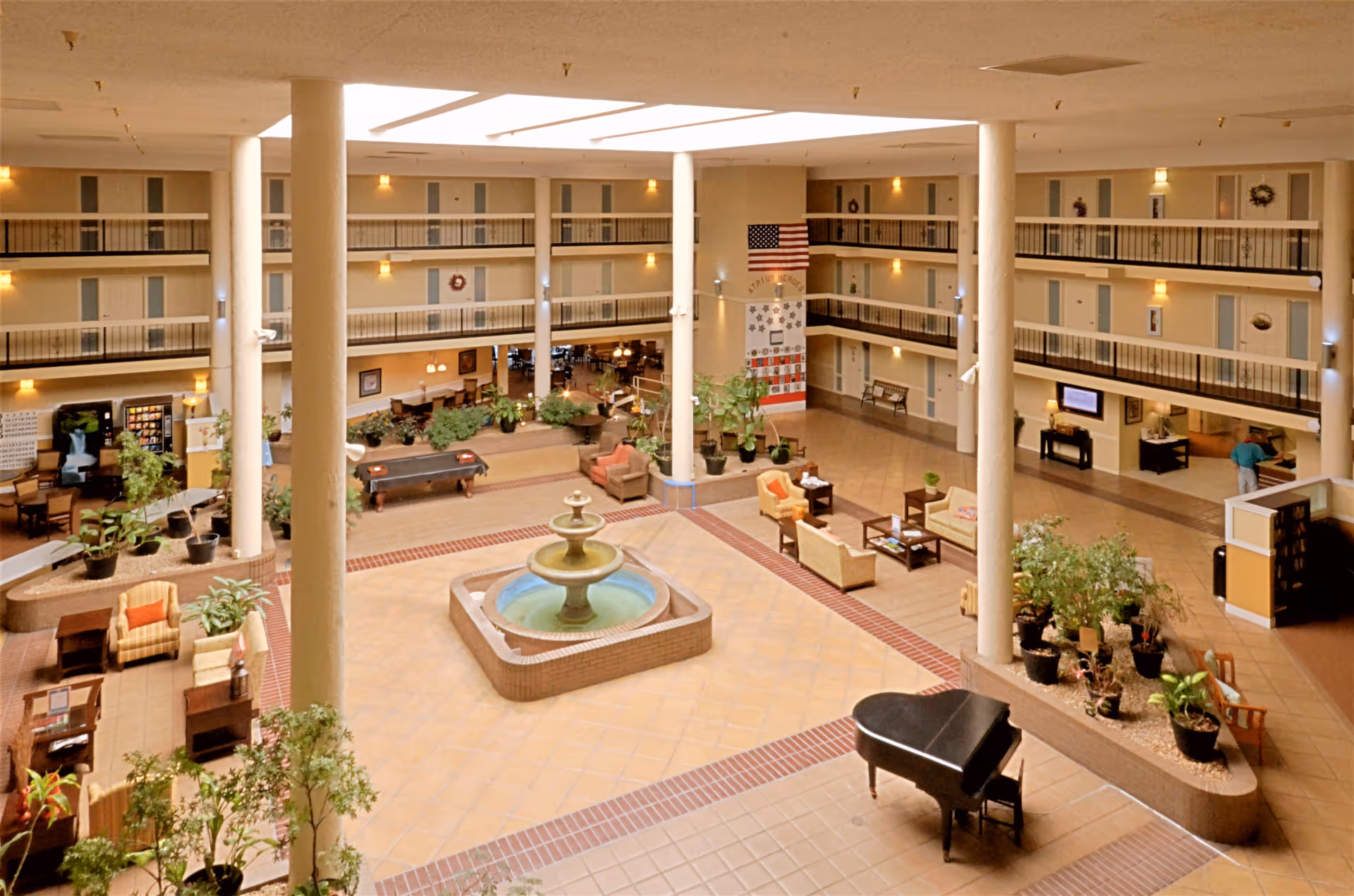 Spacious multi-level atrium with a central fountain, seating areas, plants, a grand piano, and surrounding balcony corridors.