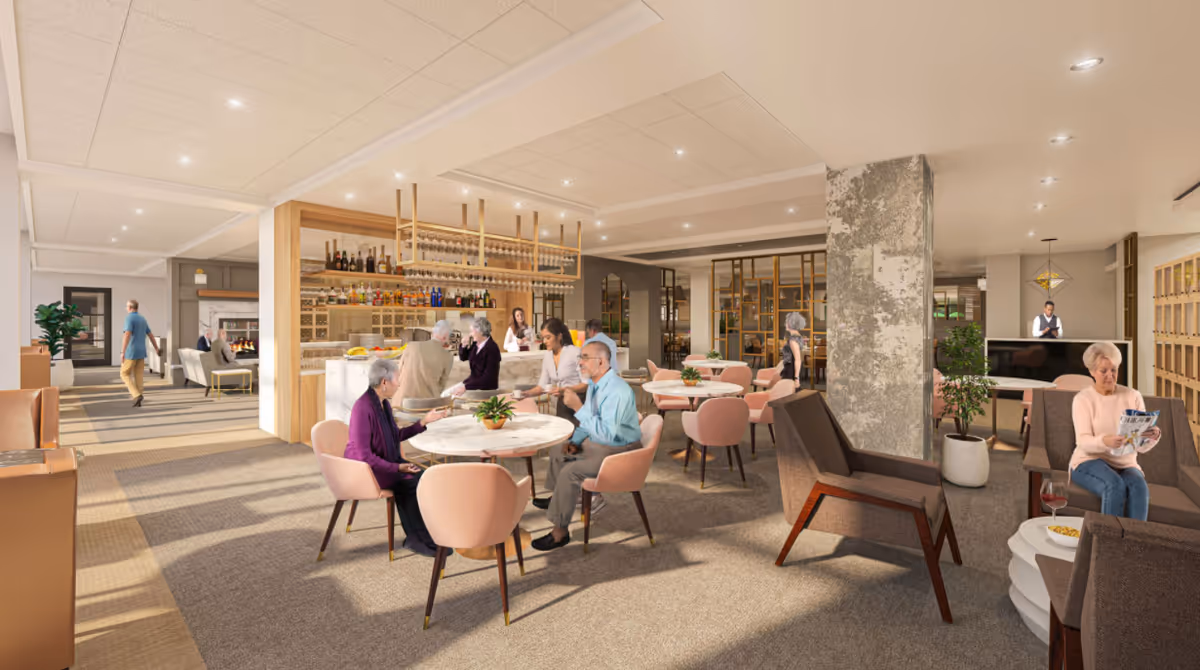 A bright communal dining and lounge area with round tables, a bar, and people seated and socializing.
