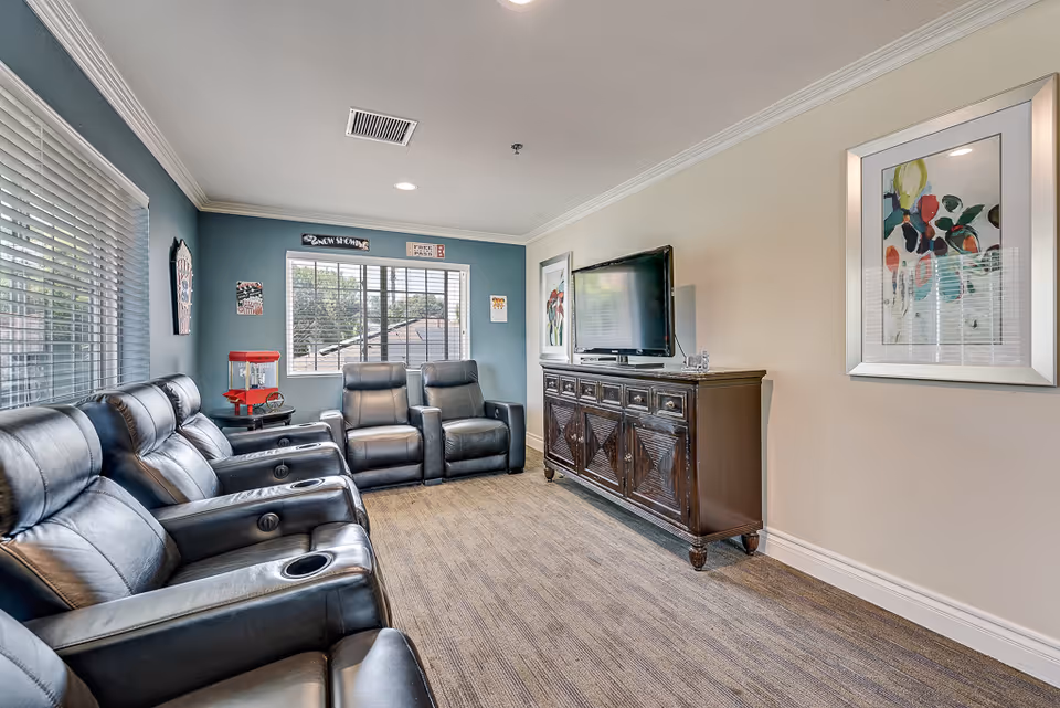 A cozy media lounge with leather recliner seats in rows facing a flat-screen TV on a wooden console.