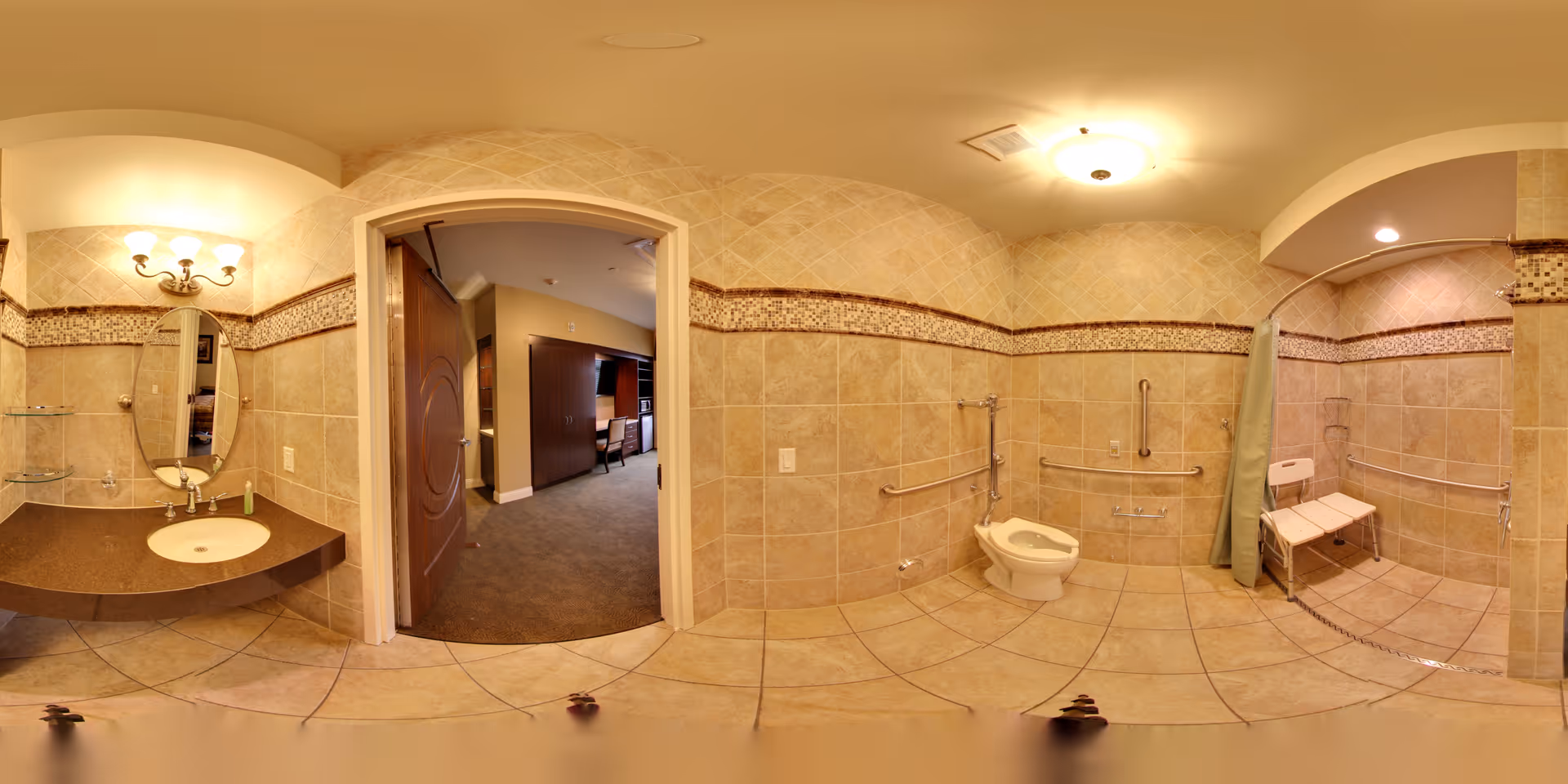 Wheelchair-accessible tiled bathroom with sink and mirror, grab-bar-equipped toilet, and roll-in shower with a shower chair, open to a hallway.