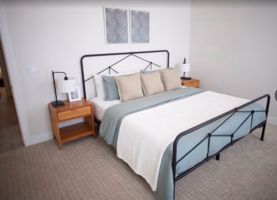 Modern bedroom featuring a metal-framed bed with pillows and bedside tables with lamps.