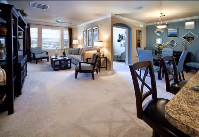 Open living room and dining area with a sofa, armchairs, coffee table, and dining set in a bright, furnished interior.