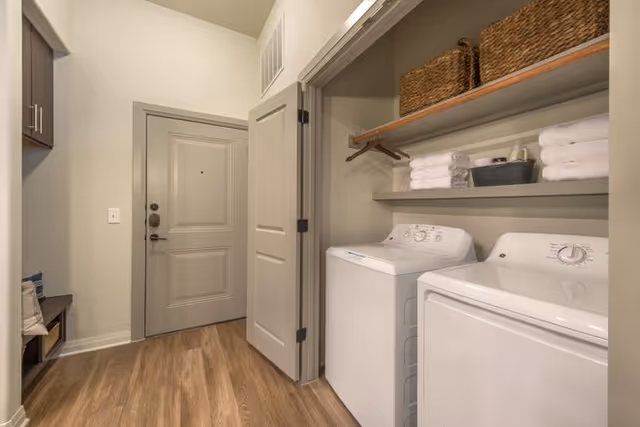 A laundry room entrance featuring a washer and dryer, shelves with towels and baskets, and a door leading outside.