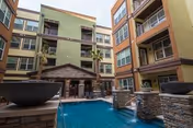 Courtyard of a multi-story senior living building with a central pool, stone water features, balconies, and an arched entry.