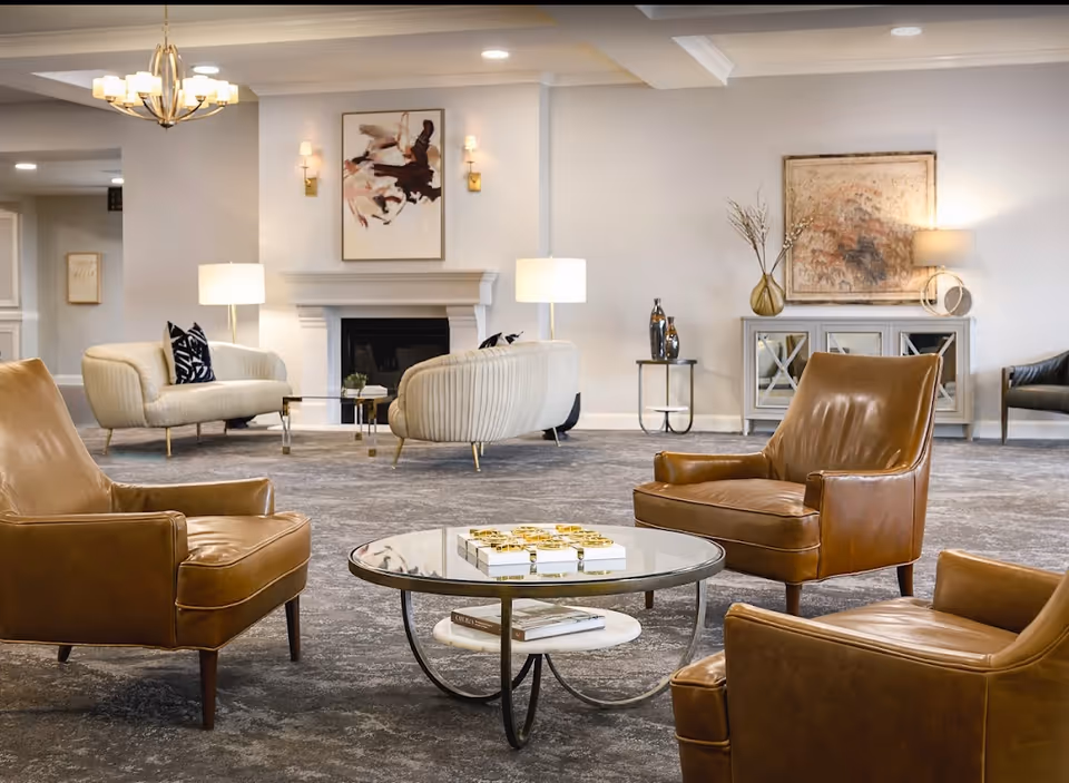 Spacious, elegantly furnished lounge with leather armchairs, a round glass coffee table, sofas, a fireplace, and ambient lighting.